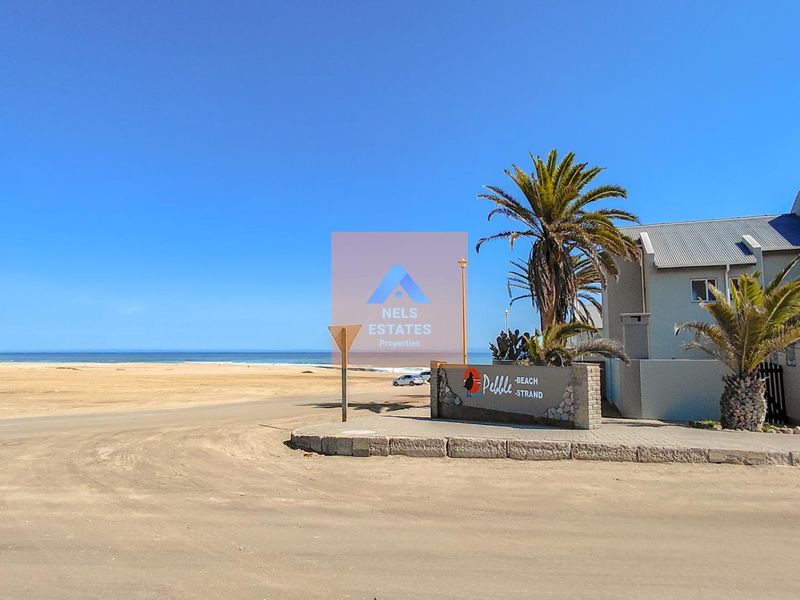 Street view of the property entrance featuring a stone-clad signage wall, palm trees, and proximity to the beach.
