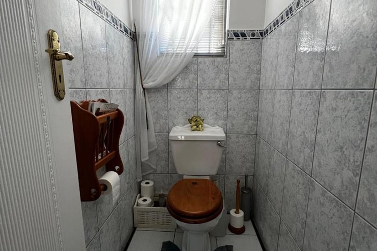A compact guest bathroom featuring floor-to-ceiling wall tiles, a standard toilet, and a small window with privacy curtain.