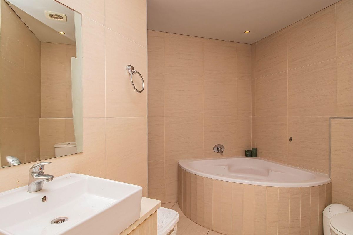 A well-maintained bathroom featuring a corner bathtub, wall-mounted basin, and neutral floor-to-ceiling tiling with recessed lighting.