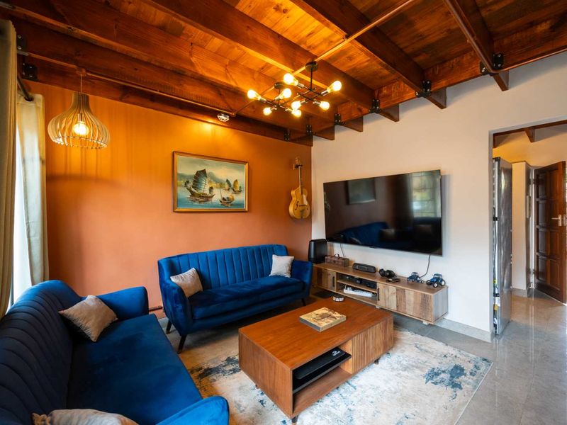 A cozy living room featuring an exposed timber beam ceiling, modern lighting, and tiled flooring, creating a warm and inviting atmosphere.