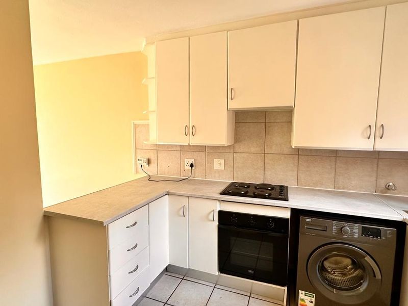 A functional kitchen featuring white cabinetry, laminate countertops, a tiled backsplash, and integrated electric cooking appliances with tiled flooring.