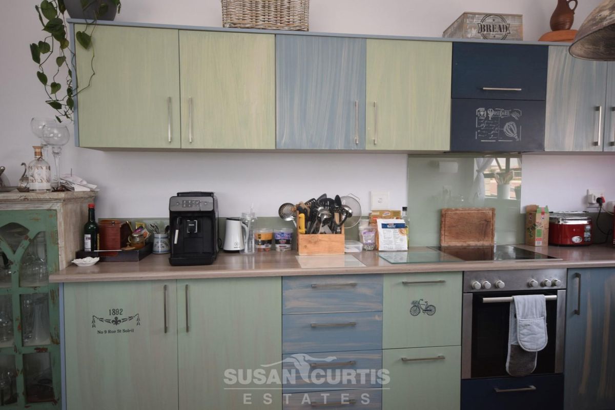 A kitchen featuring custom-painted cabinetry in blue and green tones, integrated oven, electric hob, and glass splashback.