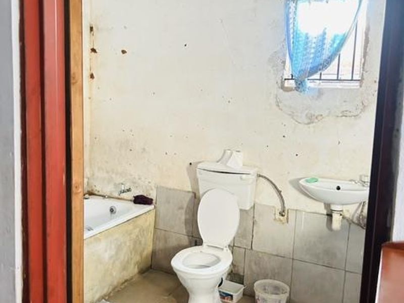 A dated bathroom featuring a built-in bathtub, toilet, and wall-mounted basin, requiring significant renovation and cosmetic updates to the walls and finishes.
