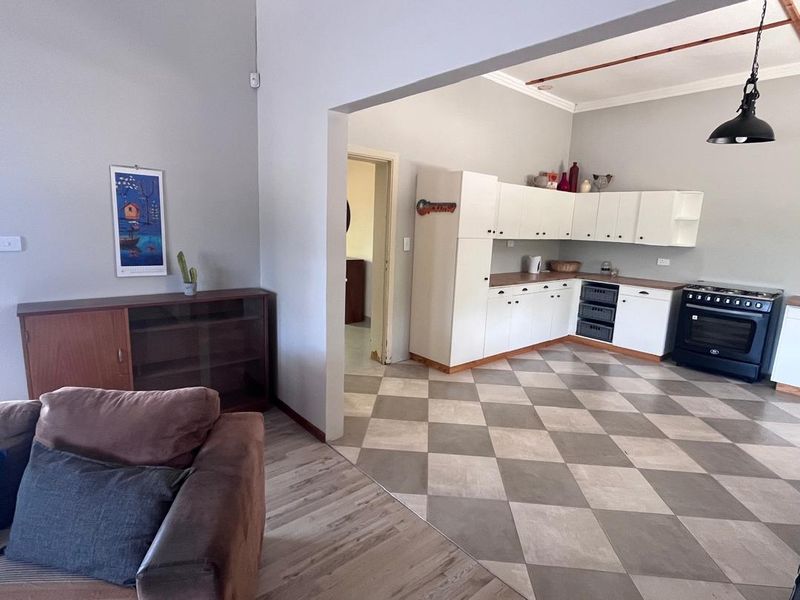 Open plan living and kitchen area featuring white cabinetry, contrasting checkerboard floor tiles, and wood-look laminate flooring in the living space.
