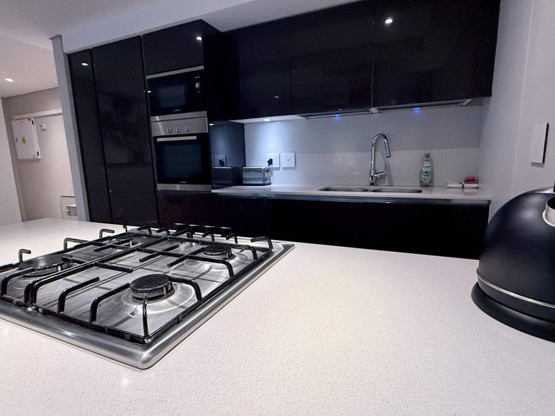Modern kitchen featuring high-gloss cabinetry, stone countertops, a central gas cooktop, and integrated stainless steel appliances.