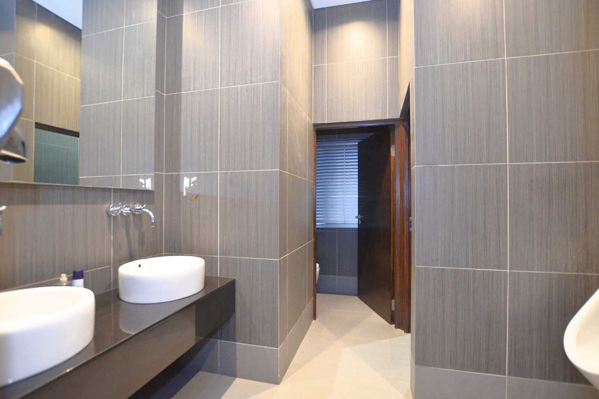 Modern office bathroom featuring dual vessel sinks, a floating vanity, large wall mirror, and contemporary grey tiled finishes.