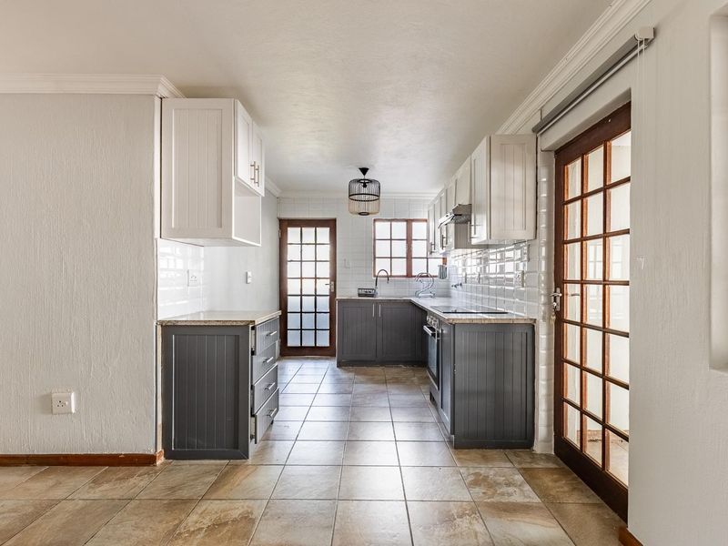 A clean, functional kitchen featuring two-tone cabinetry, stone countertops, subway tile backsplash, and direct access to outdoor areas through glass-paned doors.