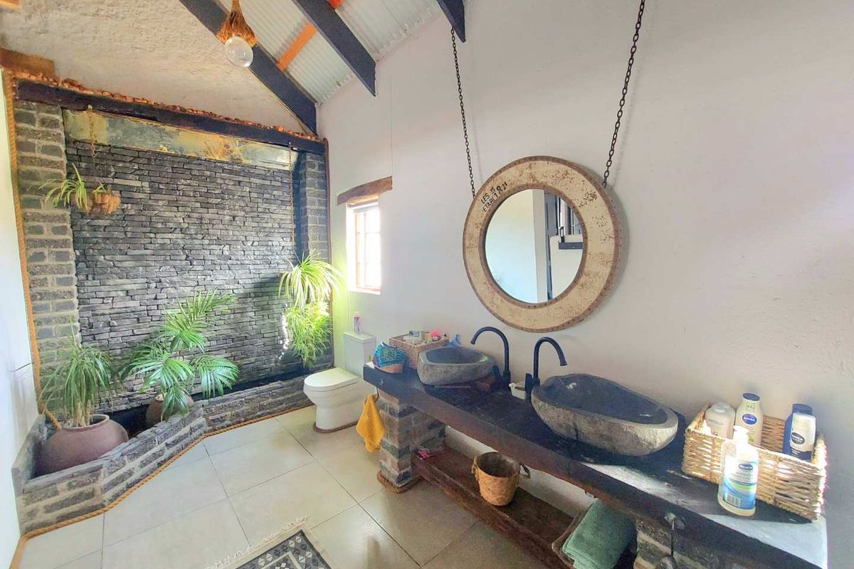 A unique bathroom featuring a stone accent wall, double stone vessel sinks on a custom vanity, and exposed timber ceiling beams.