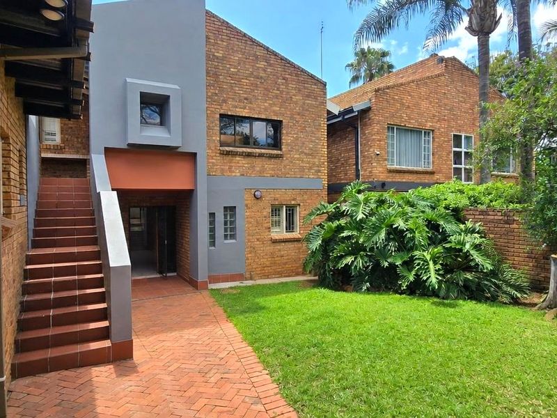Rear view of the property featuring a brick facade, external tiled staircase, paved patio area, and a well-maintained garden.