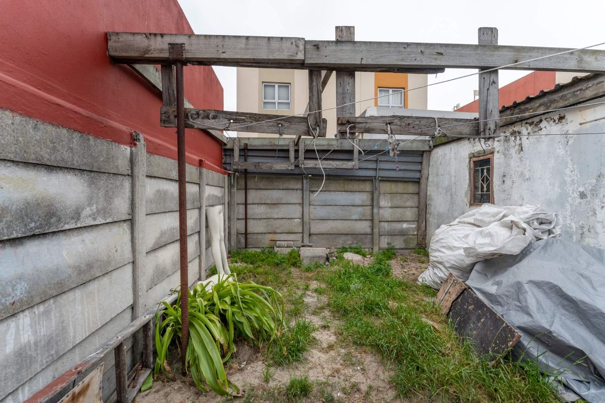 A rear outdoor area featuring a precast concrete boundary wall and a weathered timber pergola structure, requiring maintenance and landscaping.
