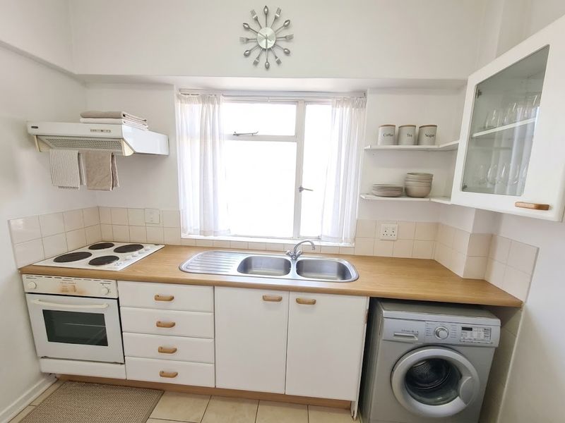 Compact kitchen featuring white cabinetry, laminate countertops, a double bowl sink, built-in oven, and electric hob with an integrated extractor fan.