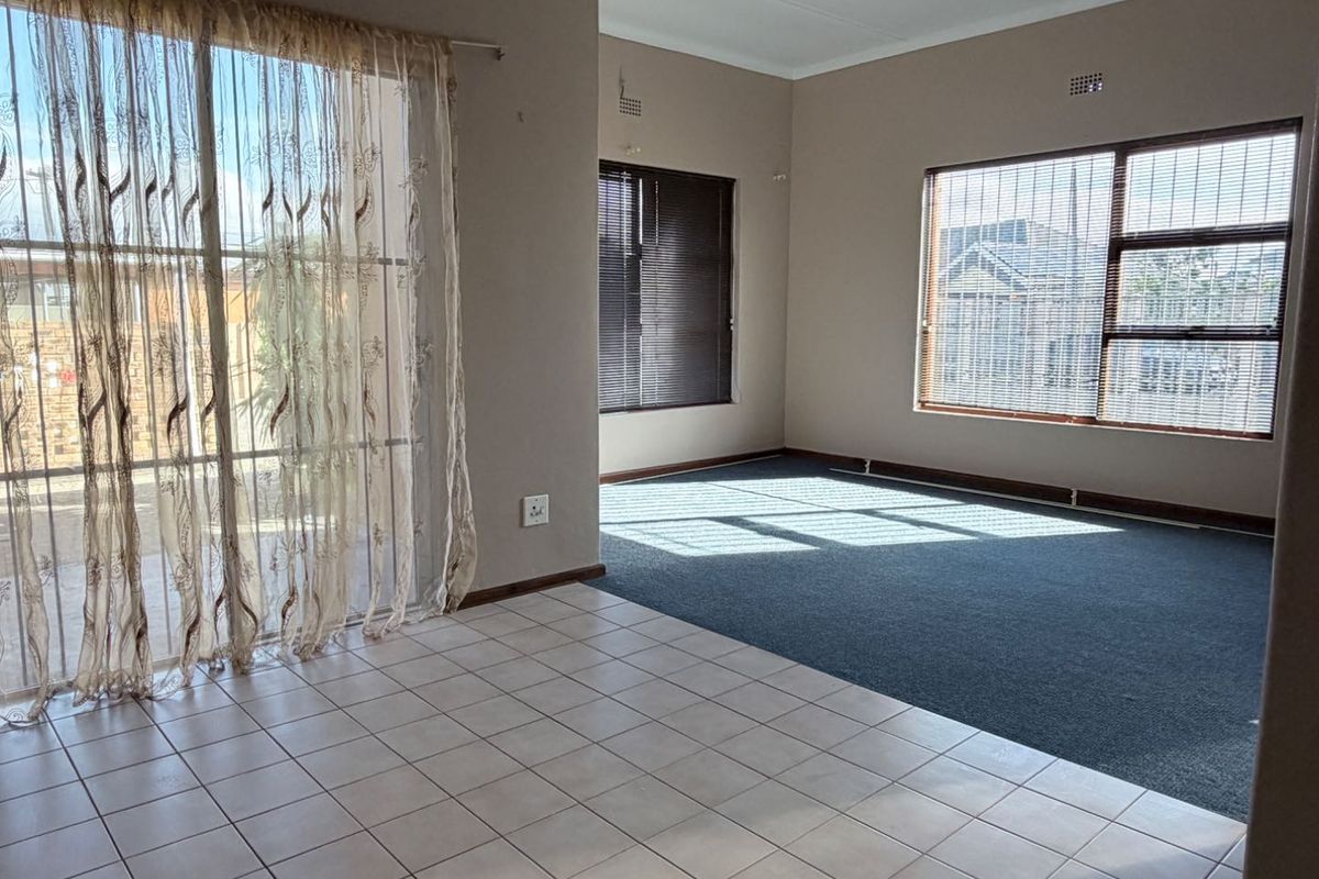 Spacious living area featuring a combination of tiled and carpeted flooring, large windows with blinds, and a sliding glass door leading to the exterior.