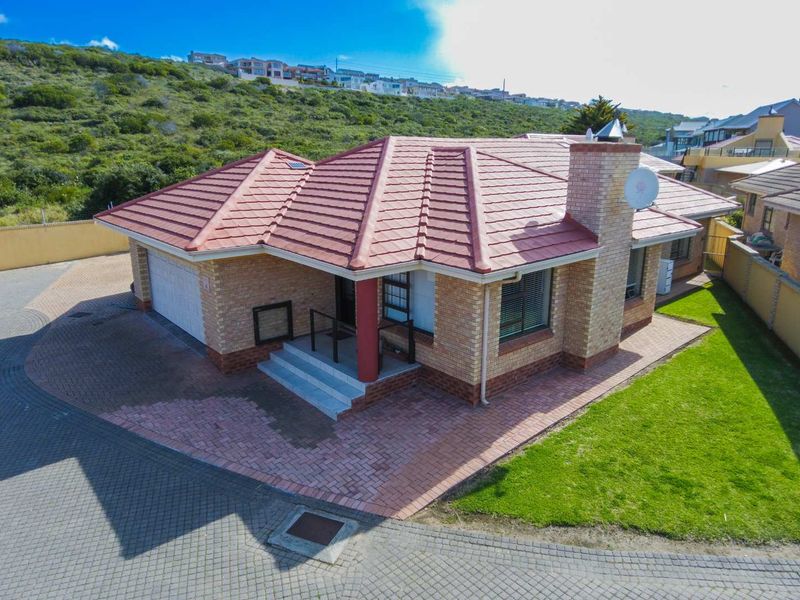 Aerial view of a single-story townhouse featuring a tiled roof, brick exterior, attached garage, and paved driveway area.