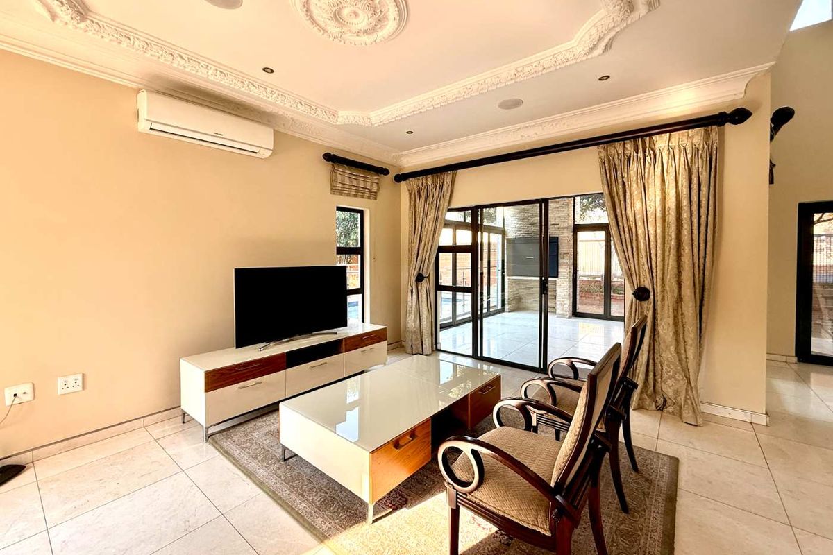 Spacious living room featuring ornate ceiling detailing, tiled flooring, and large sliding glass doors providing seamless access to the outdoor patio area.