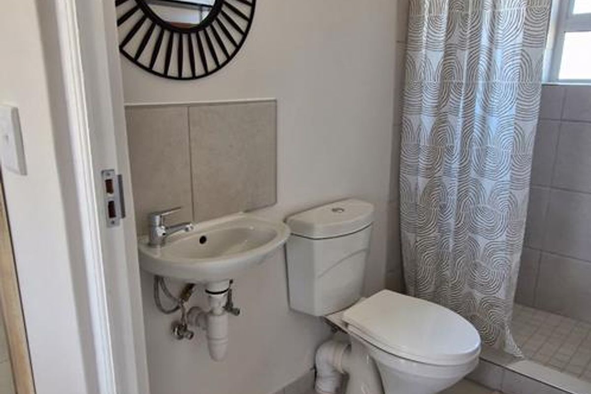 Compact bathroom featuring a wall-mounted basin, toilet, and shower area, with an exposed hot water cylinder mounted above.
