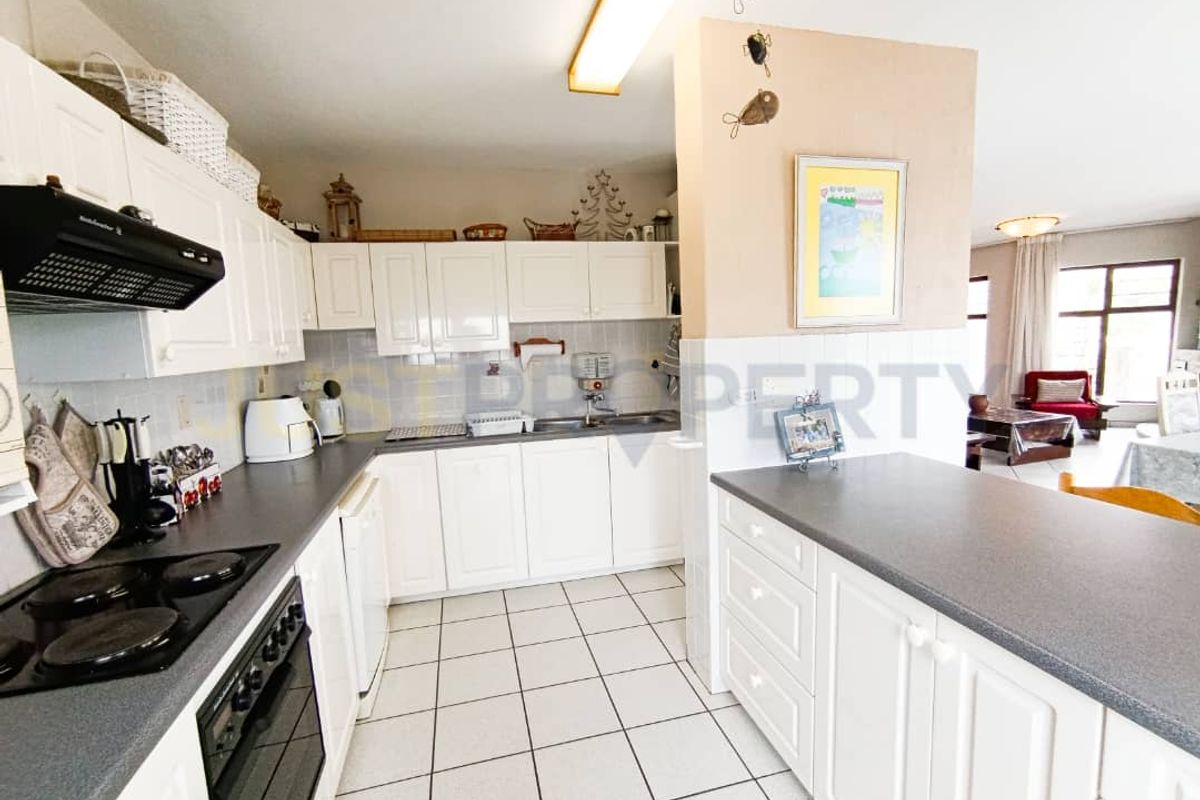 Functional kitchen featuring white cabinetry, dark laminate countertops, integrated oven and hob, and tiled flooring, flowing into an adjacent living area.