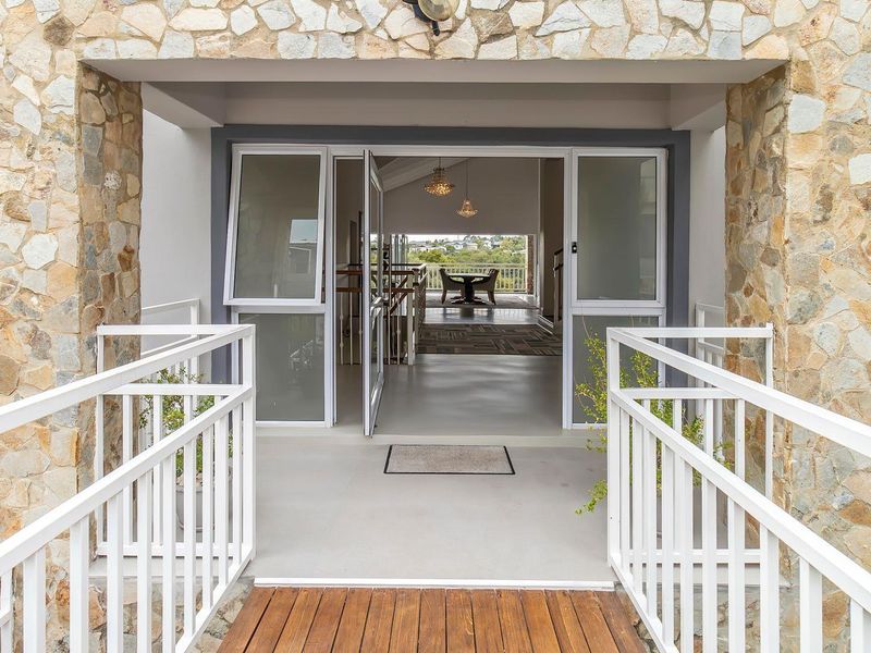 A welcoming front entrance featuring stone cladding, a wooden walkway, and a clear view through the home to the rear balcony.