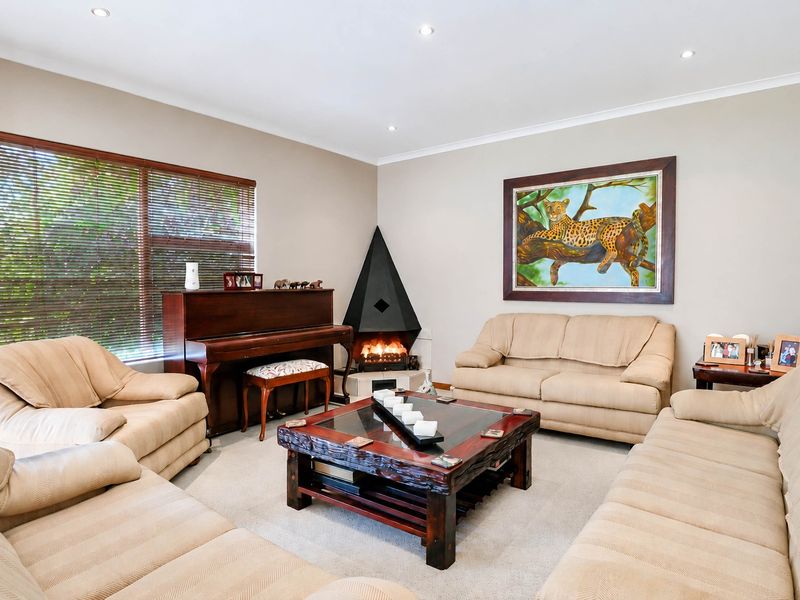A well-maintained living room featuring a unique corner fireplace, recessed downlighting, and large windows with venetian blinds.
