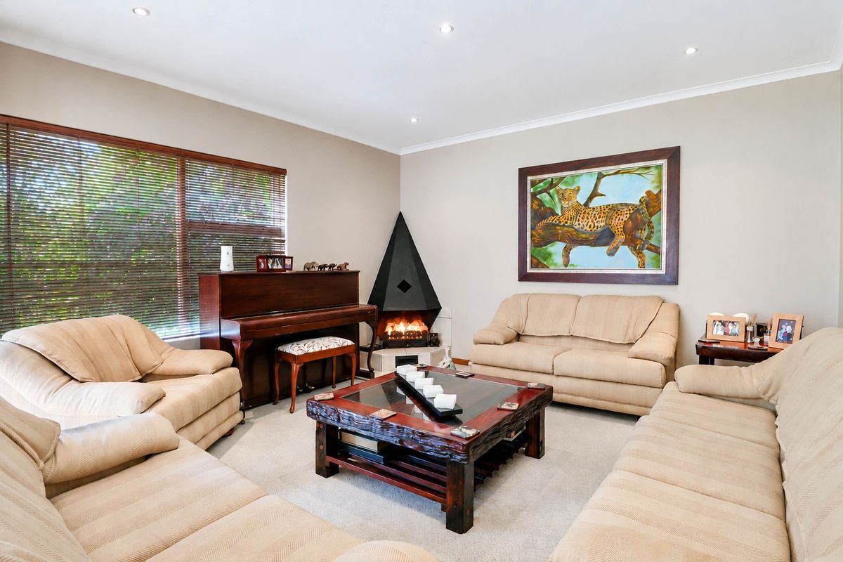 A well-maintained living room featuring a unique corner fireplace, recessed downlighting, and large windows with venetian blinds.