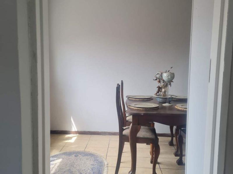A dining area featuring neutral wall tones and tiled flooring, viewed through a doorway.
