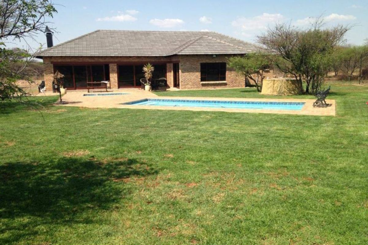 Rear view of a brick farmhouse featuring a swimming pool, paved patio area, and expansive lawn set within a rural landscape.