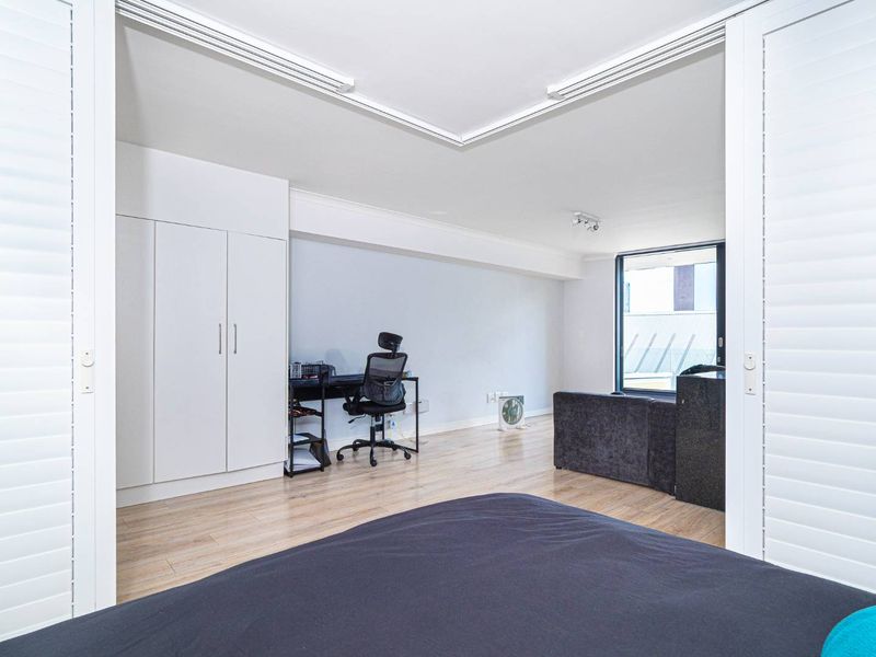A bright bedroom featuring light laminate flooring, built-in cupboards, and sliding doors that open to an adjacent living area.