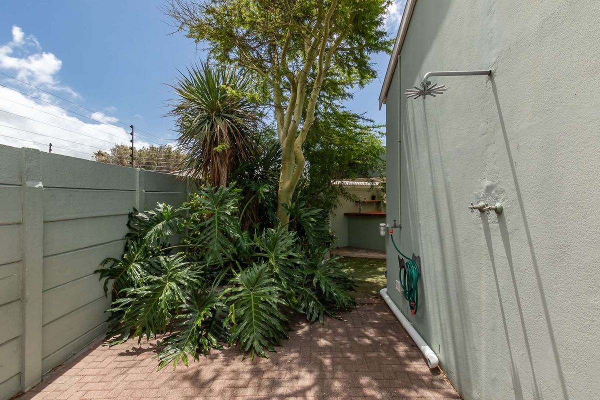Outdoor area featuring a paved courtyard, established garden, and a wall-mounted exterior shower fixture.