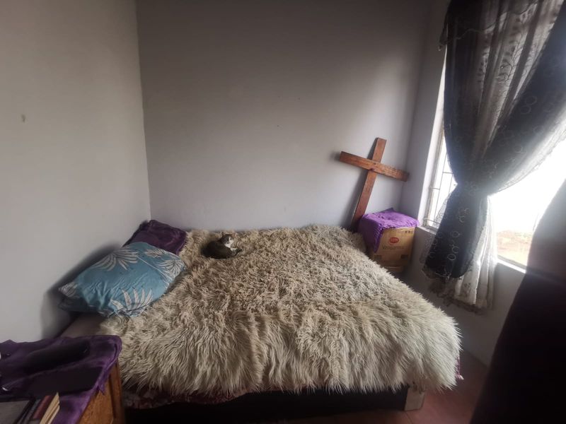 A simple bedroom featuring a window with curtains, providing natural light and a basic layout suitable for a comfortable sleeping space.