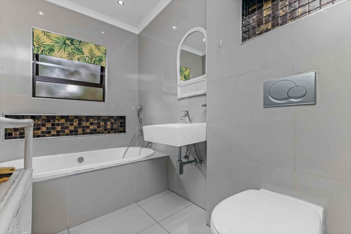 Modern bathroom featuring grey wall and floor tiles, a built-in bathtub, wall-mounted basin, and a concealed cistern toilet.