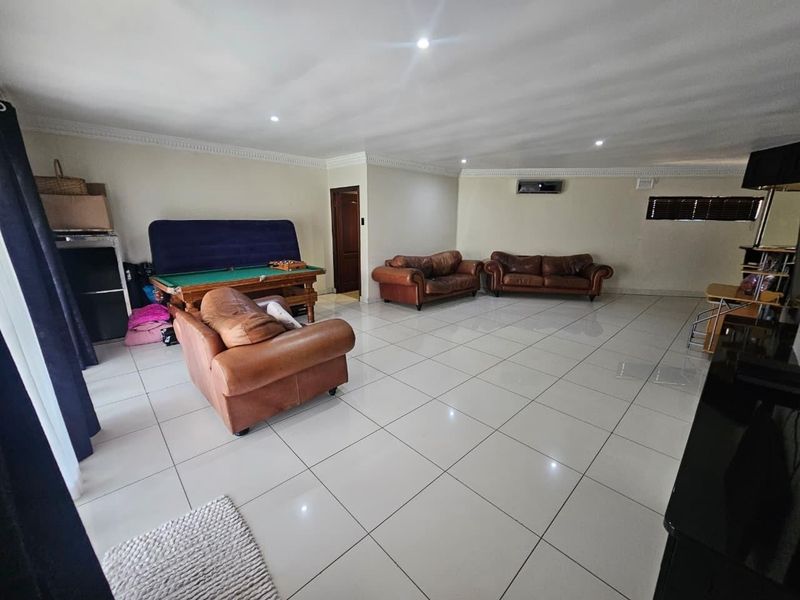 Spacious living area featuring large format ceramic floor tiles, recessed downlighting, crown molding, and a wall-mounted air conditioning unit.