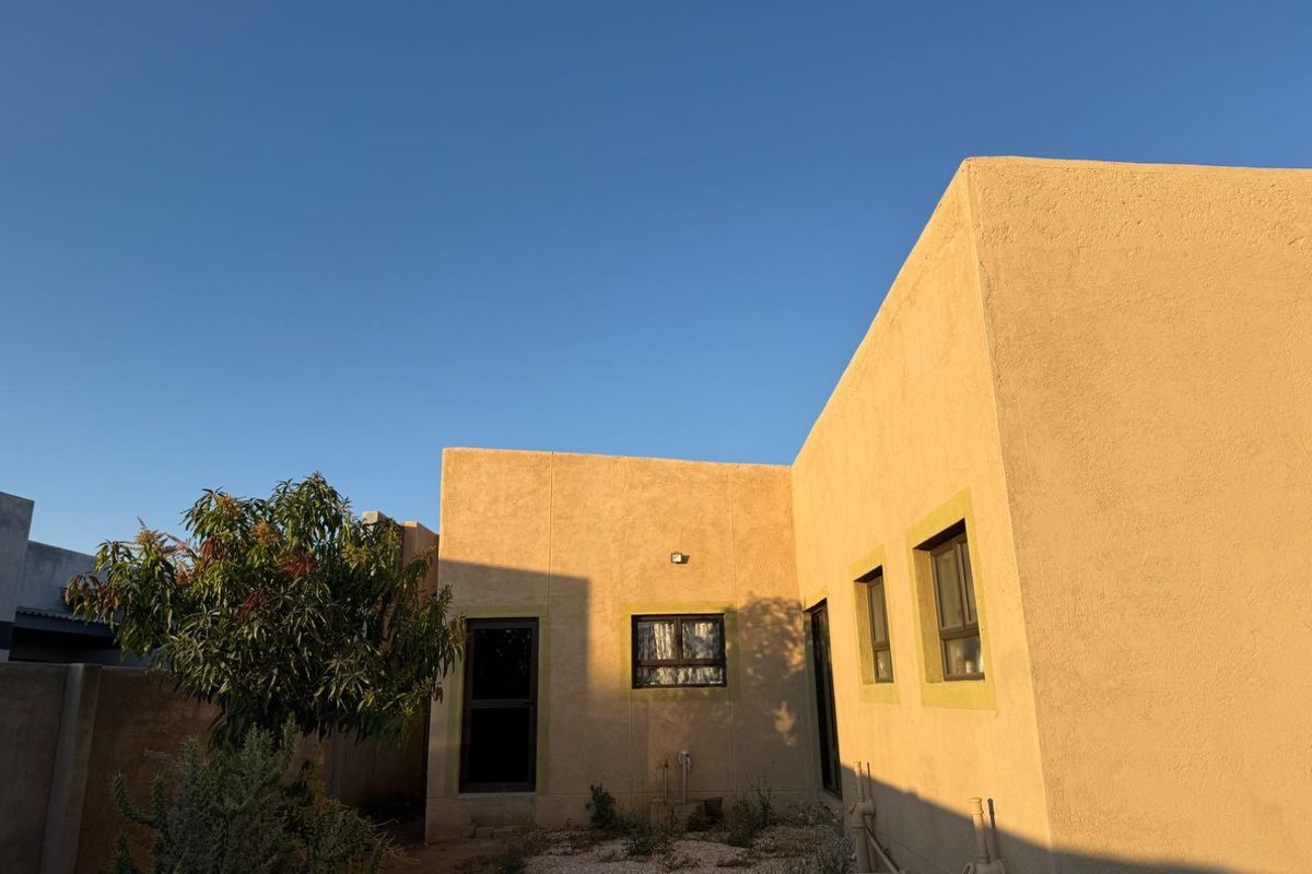 Rear elevation of the property featuring plastered walls, aluminium window frames, and a security gate, set against a clear sky.