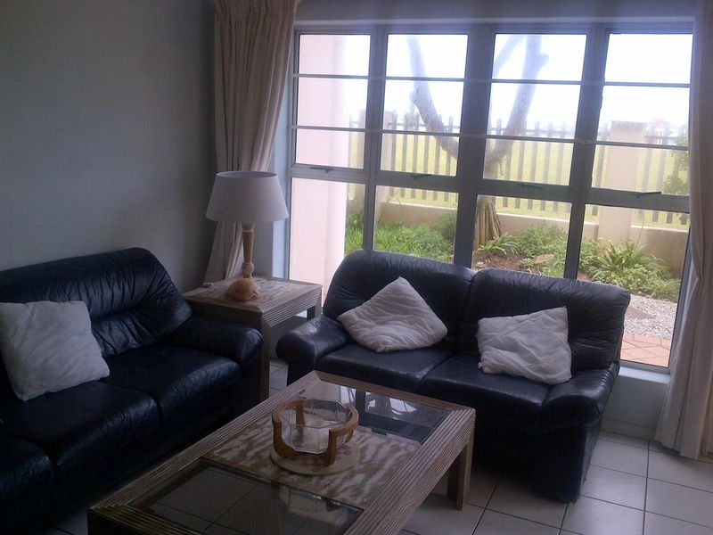 A living room featuring large aluminium-framed windows that provide natural light and a view of the outdoor garden area.