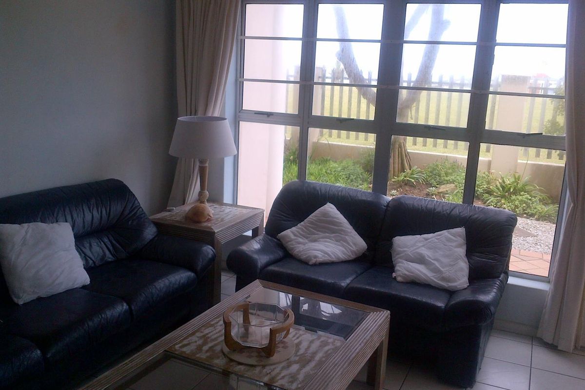 A living room featuring large aluminium-framed windows that provide natural light and a view of the outdoor garden area.
