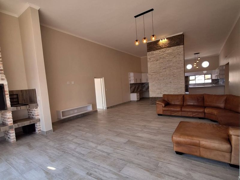 Spacious open-plan living area featuring modern tiled floors, a striking stone feature wall, and a built-in fireplace, creating a warm and inviting atmosphere.