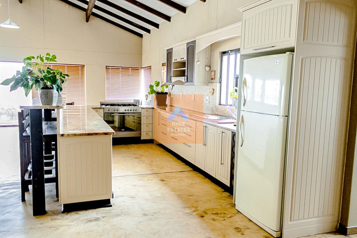 Spacious kitchen featuring white cabinetry, granite countertops, a freestanding oven, and exposed timber beams, with a breakfast bar and ample storage space.