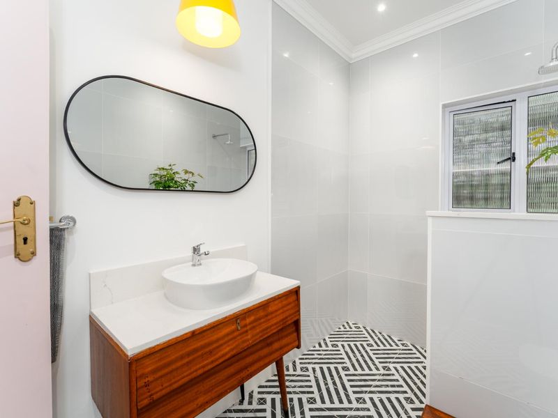 Modern renovated bathroom featuring a stylish vanity with countertop basin, patterned floor tiling, and a walk-in shower area with white wall tiles.