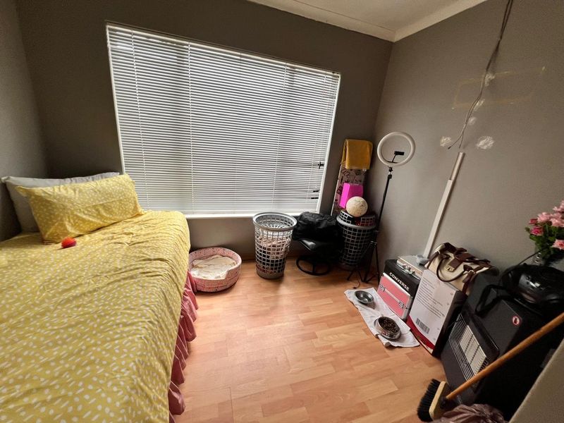 A bedroom featuring laminate flooring and venetian blinds, currently requiring cosmetic updates to the wall surfaces.