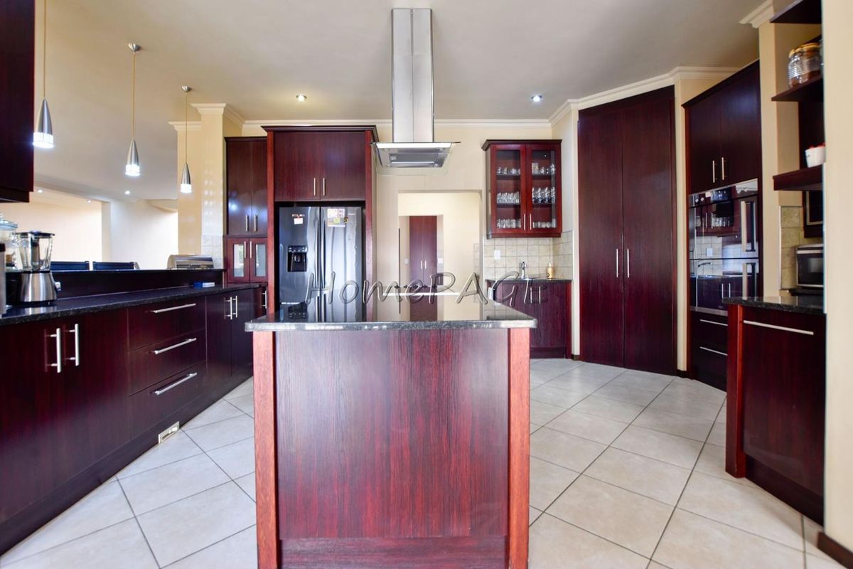 Spacious kitchen featuring dark wood cabinetry, granite countertops, a central island, and a stainless steel extractor fan.