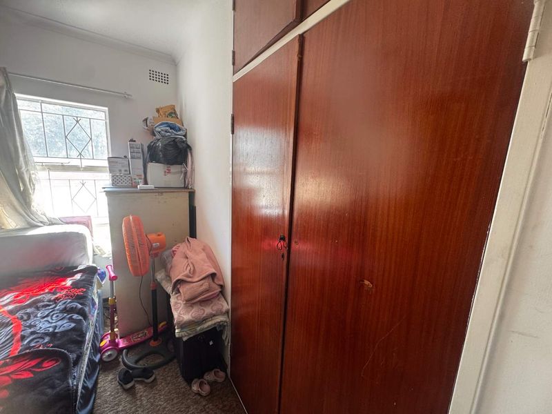 A bedroom featuring a built-in wooden wardrobe and a window fitted with security bars.