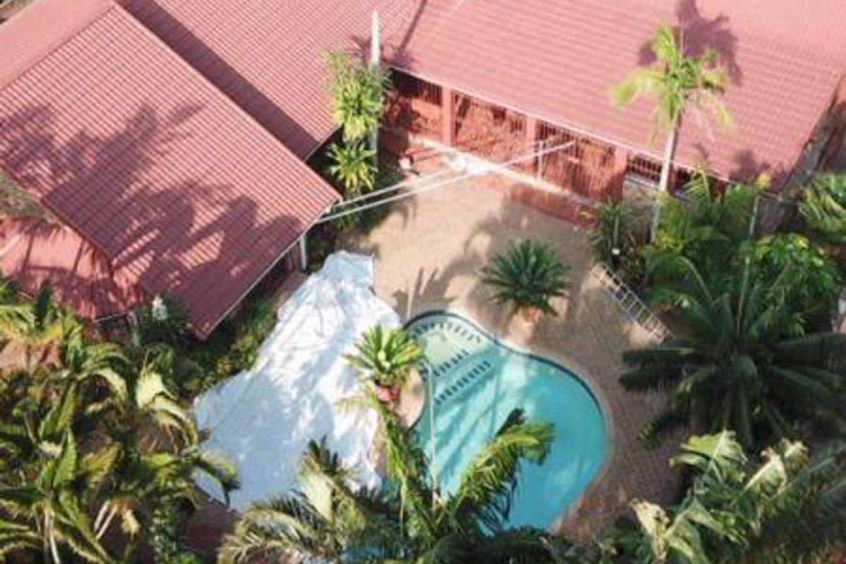 Aerial view of the property featuring a swimming pool, paved patio area, and mature garden landscaping surrounding the house with a tiled roof.
