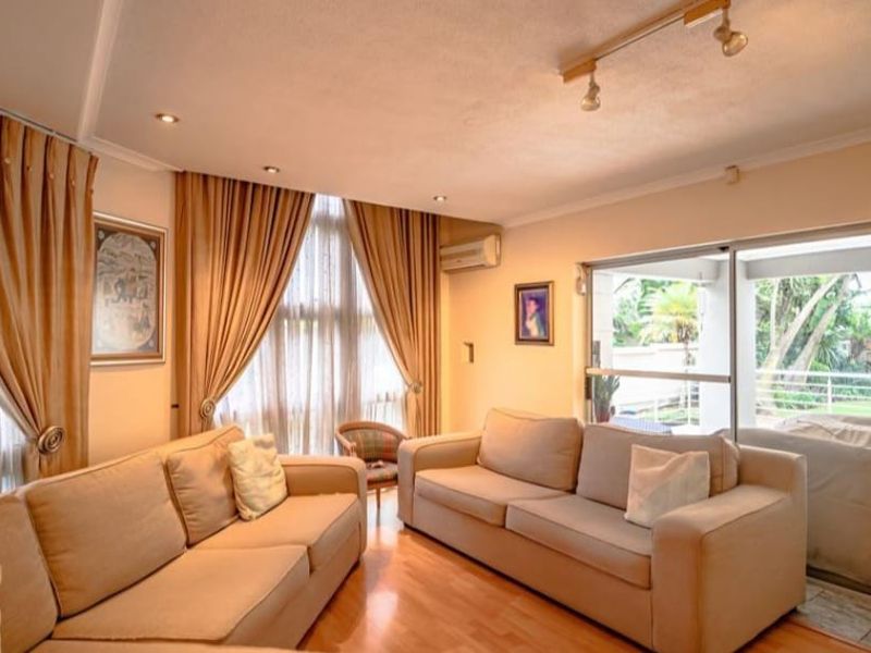 A spacious living room featuring laminate flooring, recessed lighting, and a large sliding glass door providing direct access to the outdoor patio area.