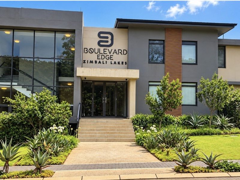 Modern apartment building facade featuring a glass curtain wall, contemporary grey exterior finishes, timber accents, and a well-maintained landscaped entrance walkway.