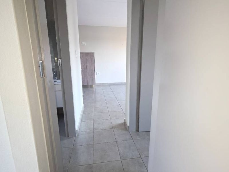 A clean, neutral-toned hallway featuring tiled flooring and access to adjacent rooms, providing a simple and functional transition space within the apartment.