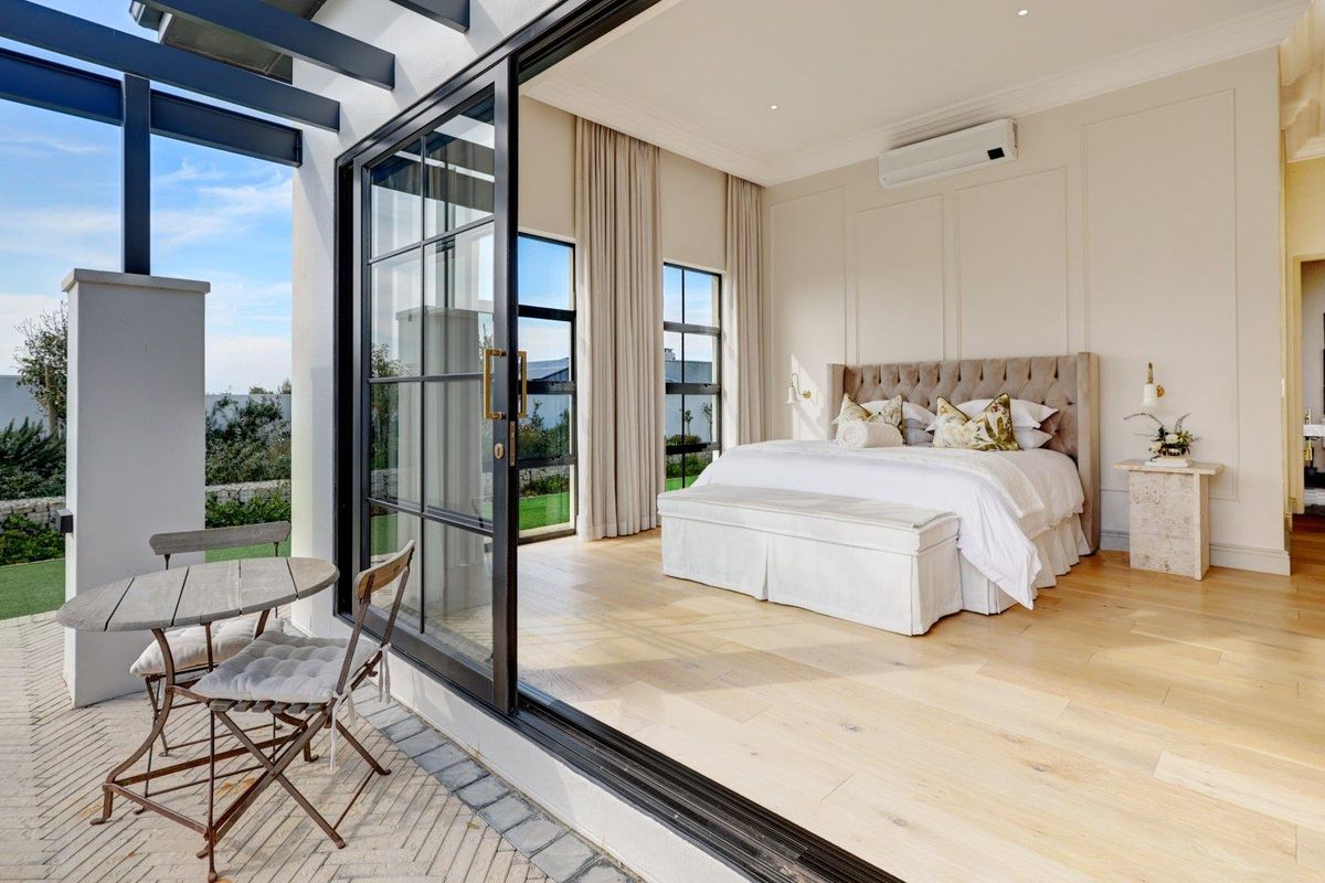 Spacious bedroom featuring elegant wall paneling, light timber flooring, and large black-framed sliding doors opening onto a private covered patio.