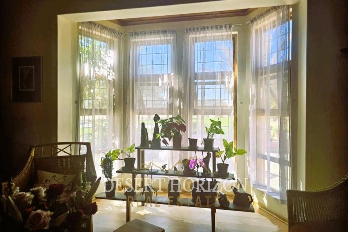 A bright living room area featuring a large bay window with leaded glass detailing, providing ample natural light and garden views.