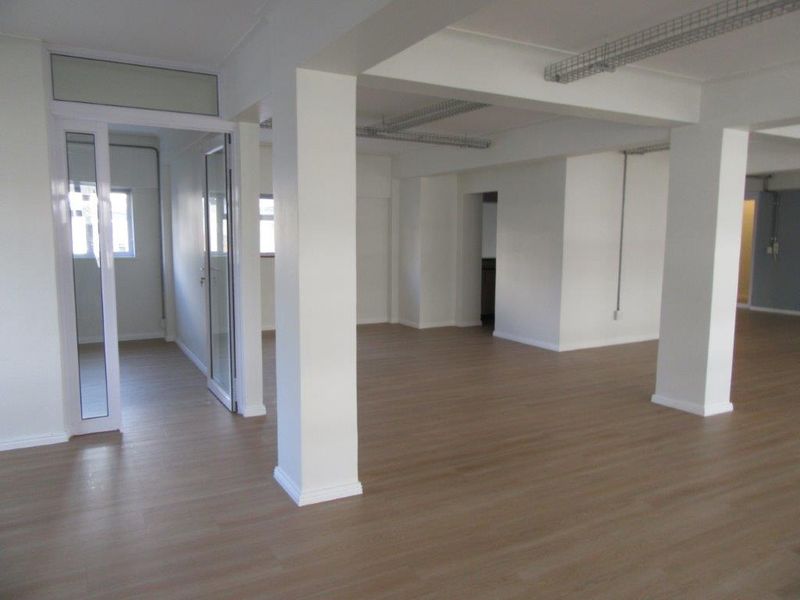 Spacious open-plan office or commercial area featuring laminate flooring, structural columns, and modern aluminium-framed glass partitioning.