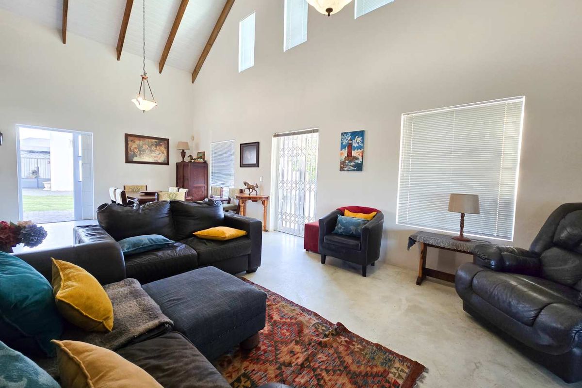 Spacious living room featuring a high vaulted ceiling with exposed timber beams, tiled flooring, and large windows with venetian blinds.