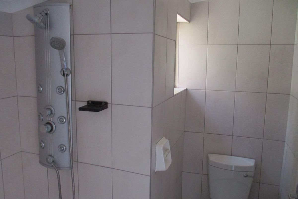 A functional bathroom featuring a wall-mounted shower panel system with multiple jets and a standard white toilet.