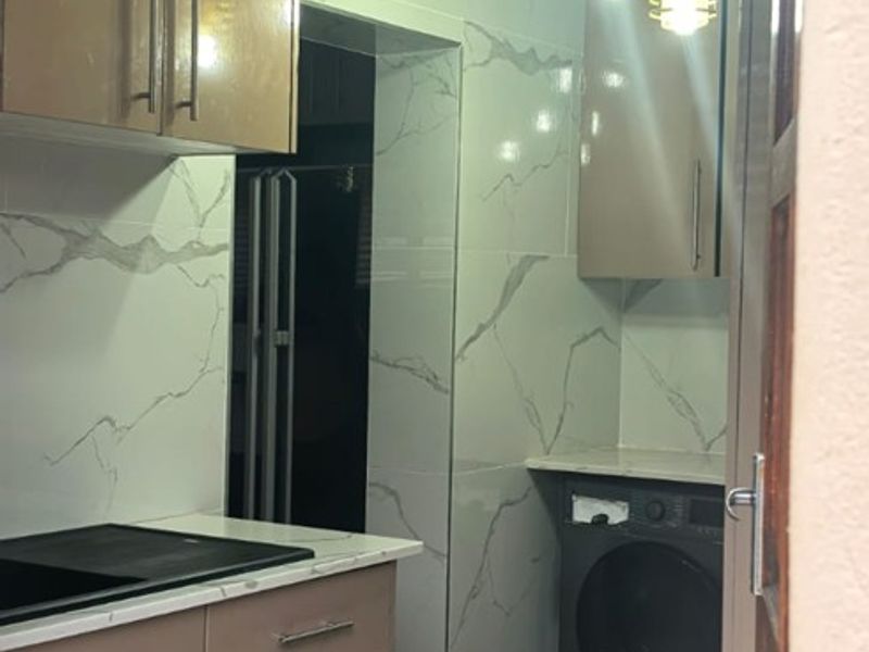 A modern scullery featuring sleek built-in cabinetry, marble-look wall tiling, and contemporary pendant lighting, providing a functional and stylish secondary kitchen or utility space.