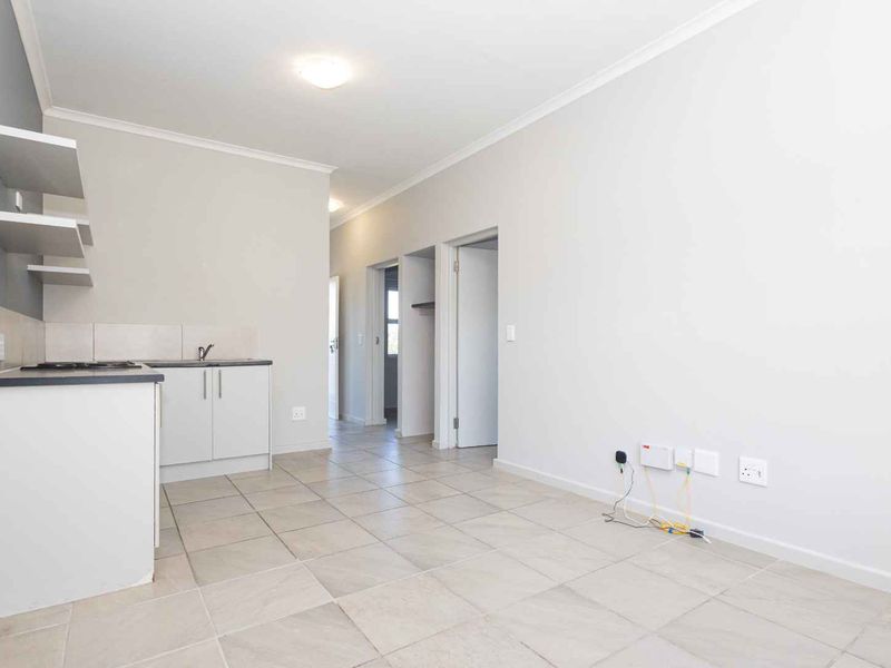 An open-plan living and kitchen area featuring neutral tiled flooring, built-in cabinetry with a hob, and clean, modern finishes throughout.